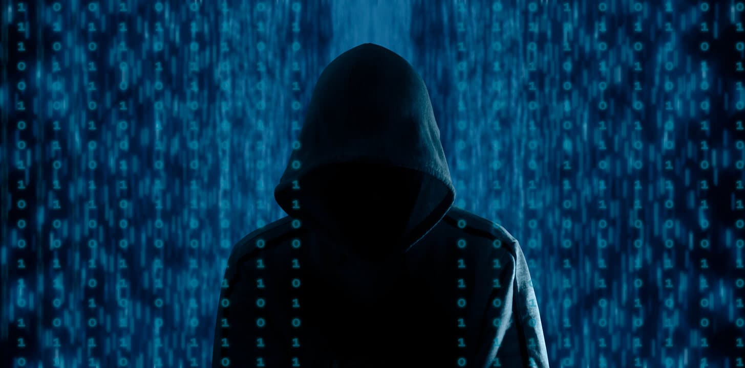Ransomware attack hacker in front of a blue screen of numbers.