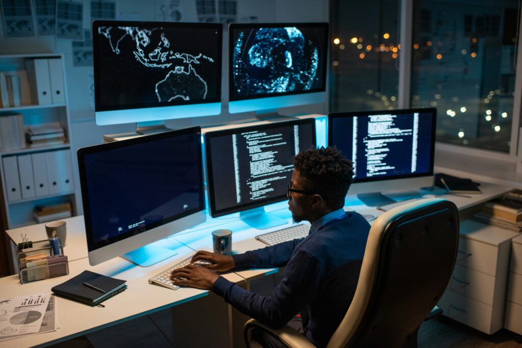 A man codes and manages his application hosting late at night on three monitors side by side