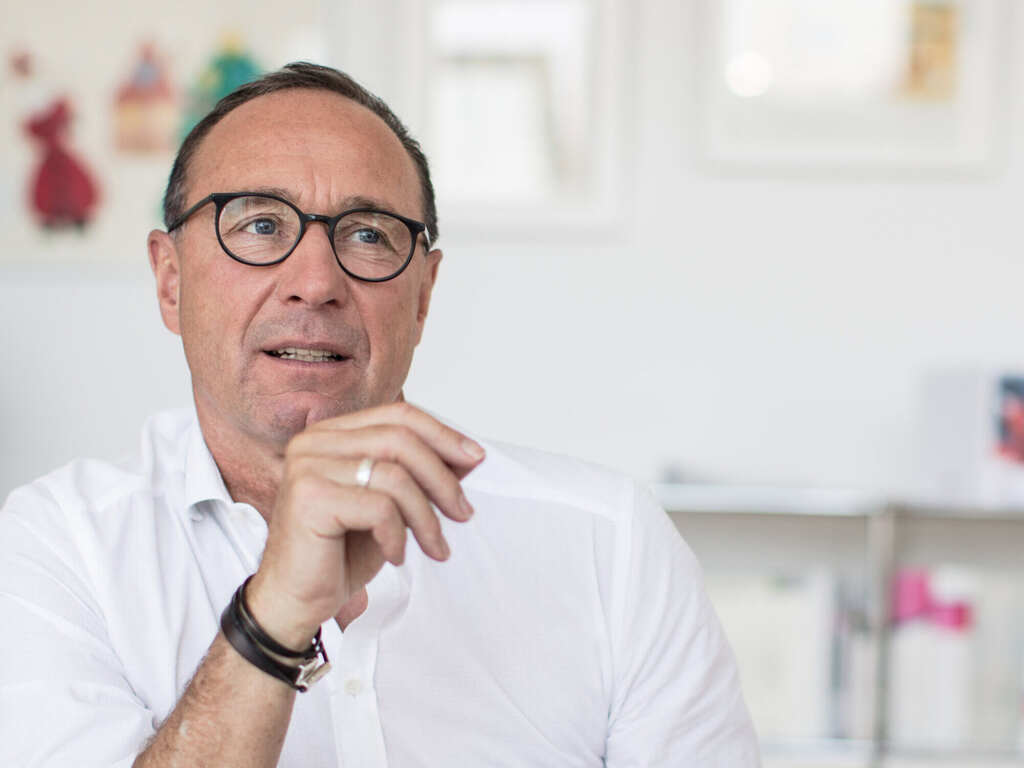 A man in glasses wearing a watch and a ring is in discussion in a modern office