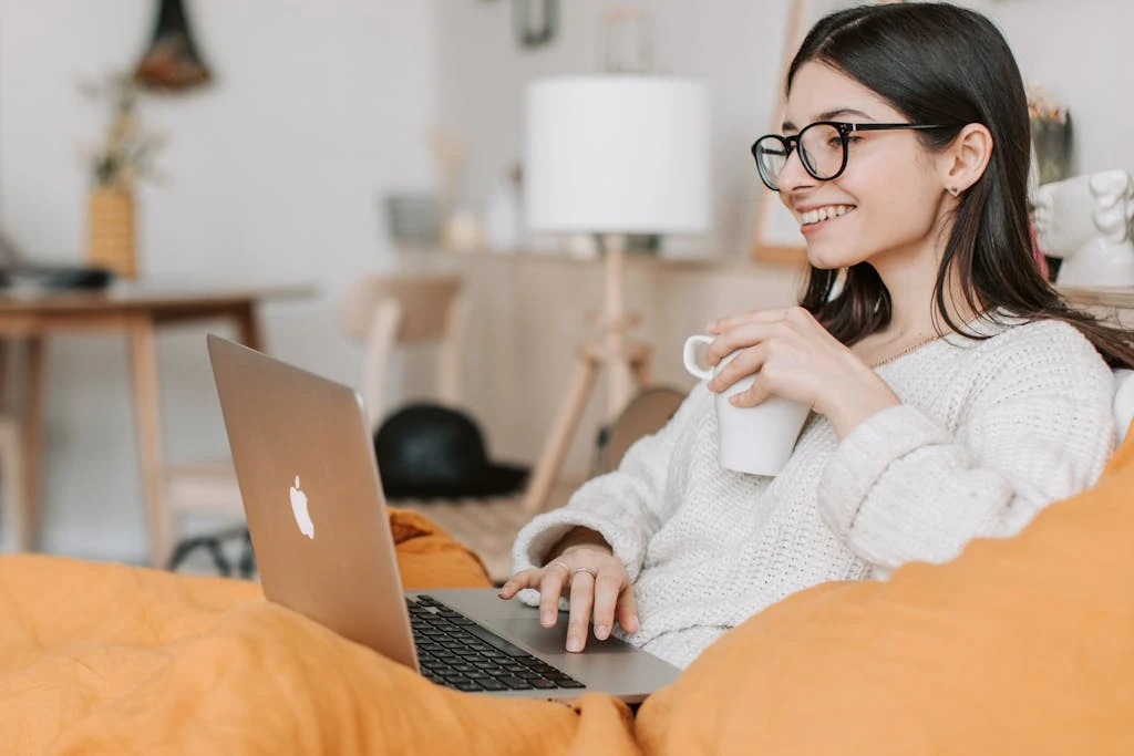 Woman Enjoying Coffee While Using Laptop On Her Orange Couch