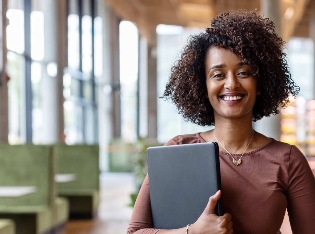 a woman web professional confidently smiles in an office environment while holding a laptop computer