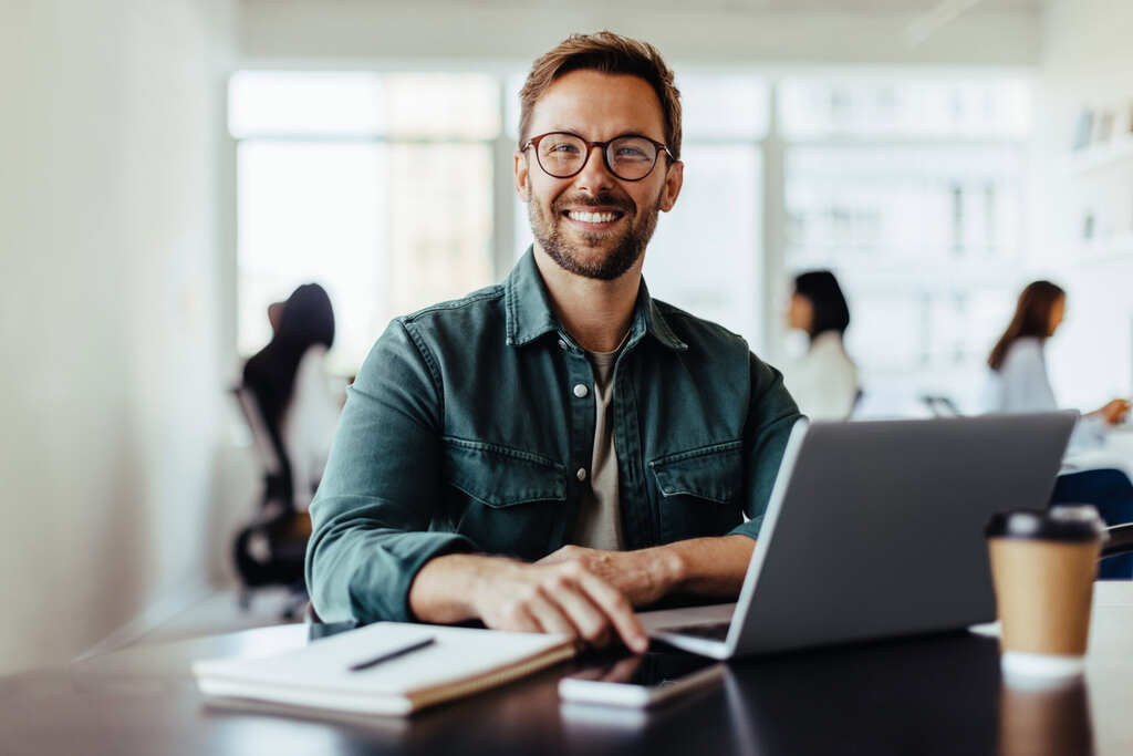 A man in a collared shirt and glasses smiles at the camera as he finishes setting up his WordPress hosting