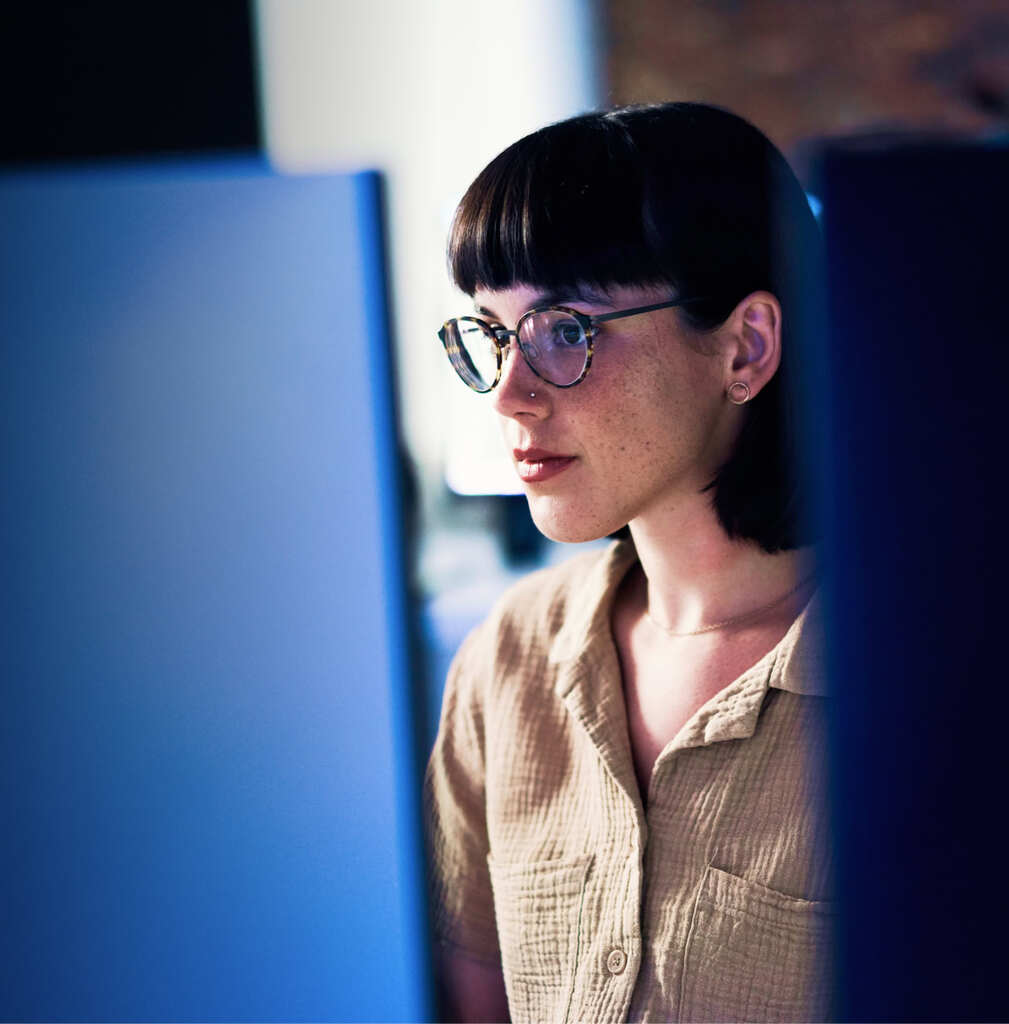 a woman with bangs and glasses studies two computer screens as she manages her cloud hosting