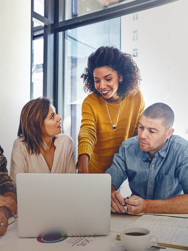 Three individuals look over a laptop in a business setting