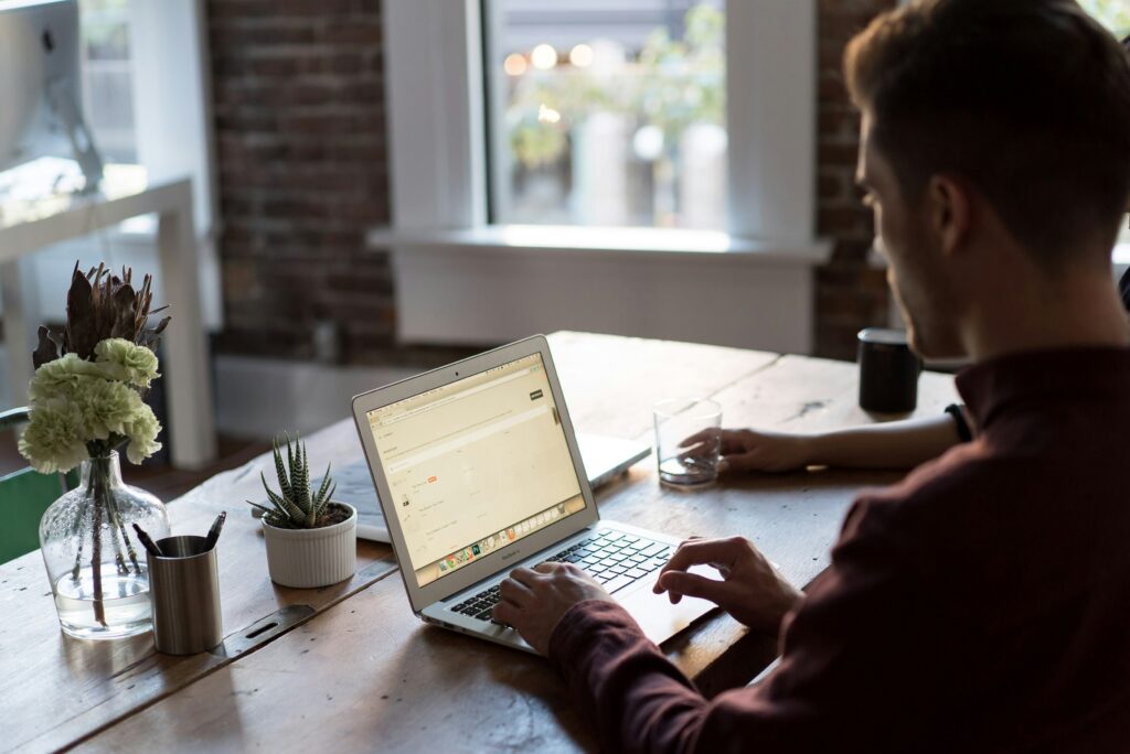 A man sets up Google reCAPTCHA on WordPress from his laptop, he sits at a desk with a glass of water, plants, and a cup holding pens