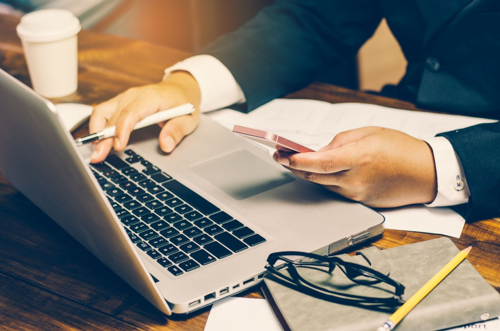 A man on his phone typing on his laptop.