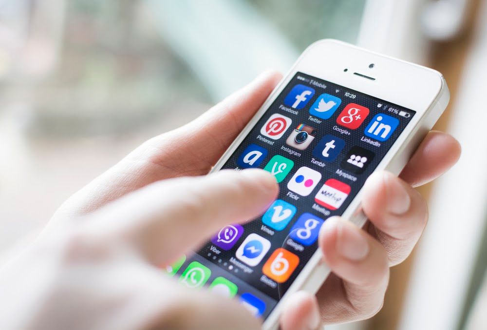 A hand holding a cell phone with a screen full of social media apps. 