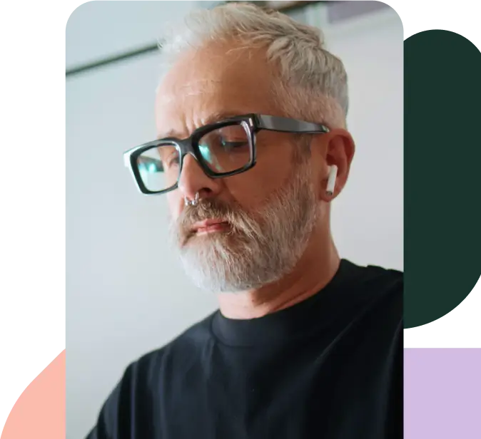 Man in glasses and a septum piercing works on his event with airpods in. 