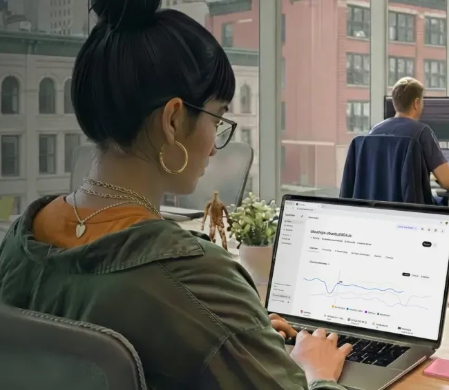 A woman in glasses monitors her hosting services in the Liquid Web portal, the screen shows resource usage over time. 