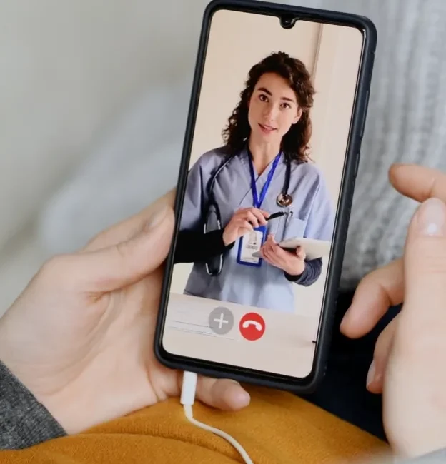 A person holds a mobile phone and video chats their doctor on an app hosted with HIPAA compliant servers.