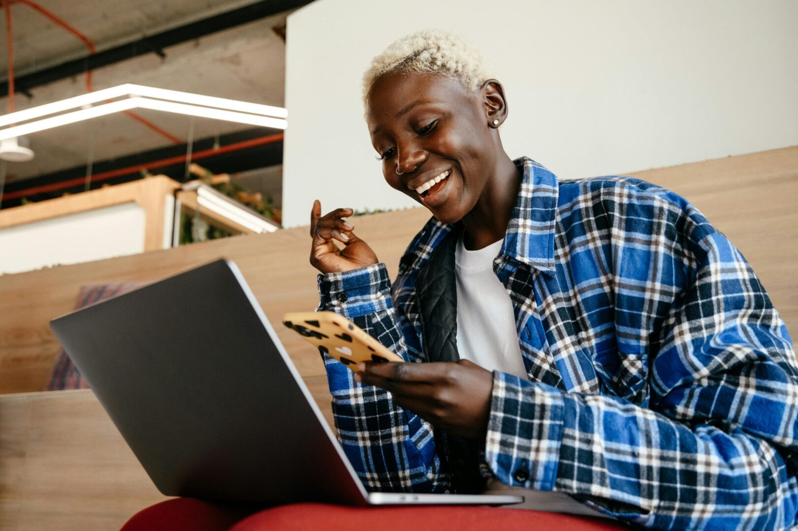 Smiling person sitting with a laptop and holding a cellphone